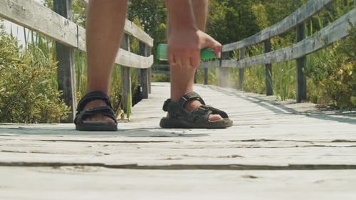 Man Sprays Insect Repellent on Legs on Wooden Bridge
