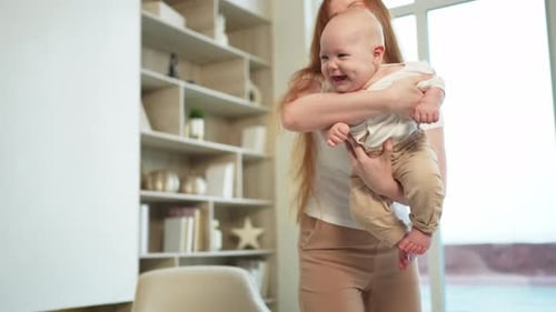Happy Mother Holding Laughing Baby at Home