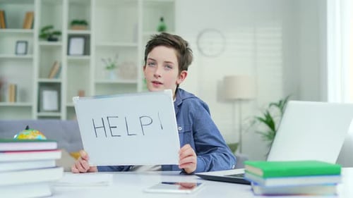 Portrait of a tired schoolboy who sits and teaches lessons at the table at home. Showing a board 1