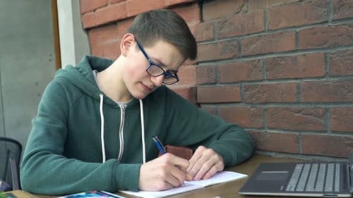 Young, Teenage Boy with Notepad Doing Homework by Table in Cafe Adolescent