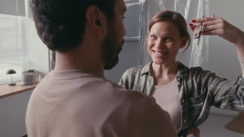 Happy Young Couple Embracing after Woman Showing Key to Her Husband