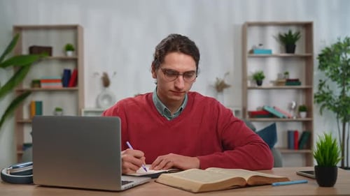 Young Adult Man Spending Time at Home Man Student Sits at Desk Works on Laptop Writing Text in