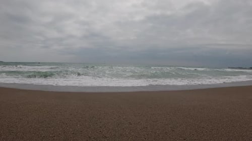 Ocean waves gently crash onto a sandy beach beneath a dramatic cloudy sky.