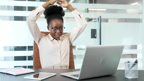 Happy african american businesswoman finished work on laptop while sitting at workplace in office.