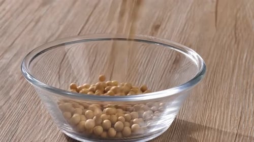 Soybeans being Poured Into Glass Bowl on Wood