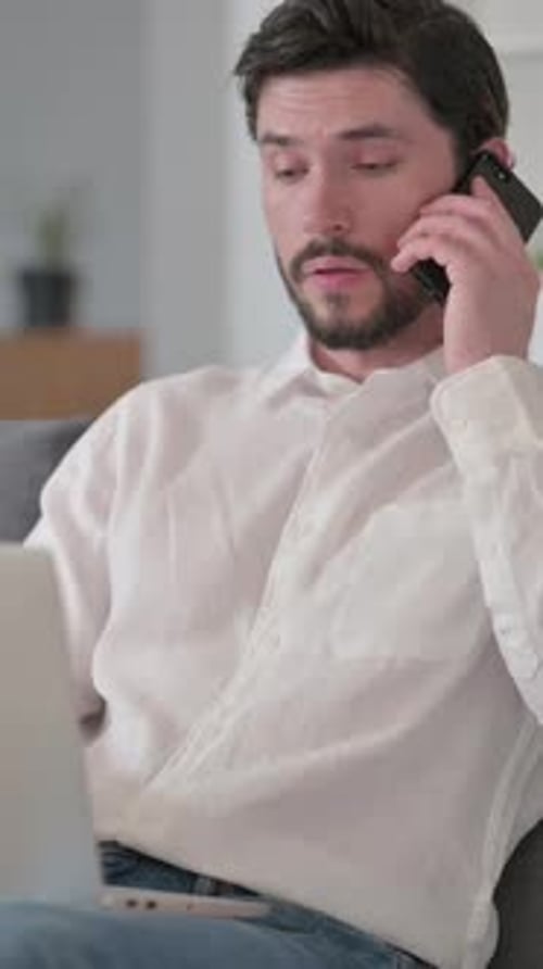 Man on Phone While Using Laptop Indoors