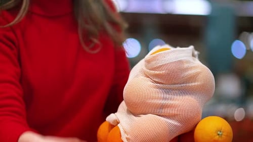 Mujer recogiendo naranjas en una bolsa reutilizable en una tienda. Temáticas del Día de la Tierra y la Ecología