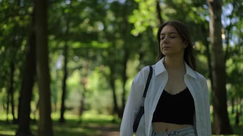 A Girl Leisurely Walks Through the Park on a Sunny Summer Day and Looks Around