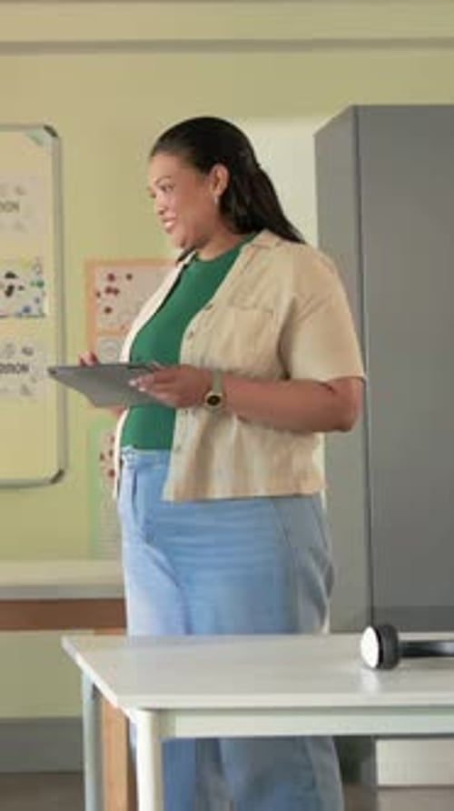 Vertical video: Reacting to left student thumbs up, teacher in green top reading tablet class front