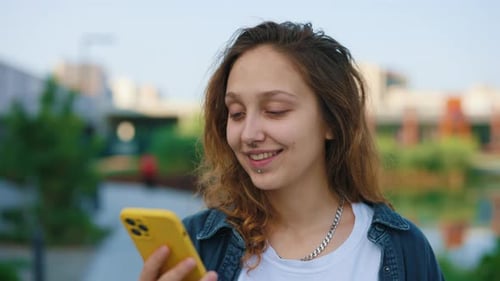 Beautiful Caucasian Woman Walking Outside Using Smartphone Standing Near the Local Lake Texting