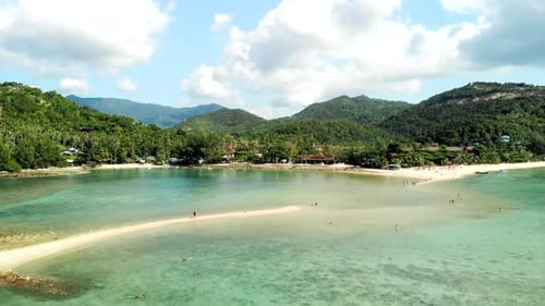 A drone flight over clear waters beach with mountains in the background