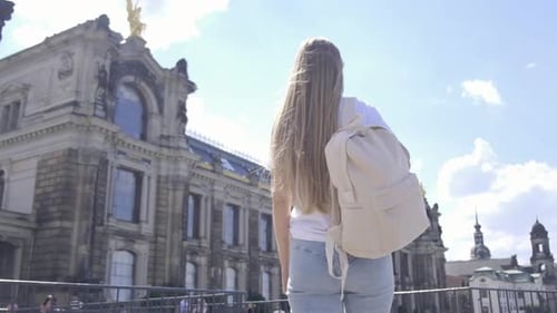 Woman Backpacking in a City Gazing at Skyscrapers Against Cloudy Sky