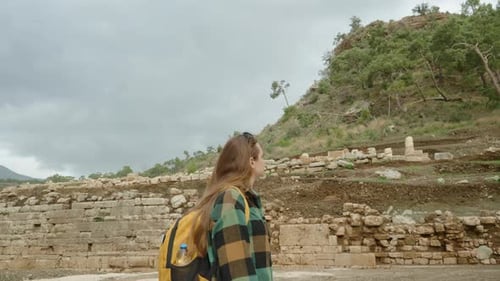 Young woman with an orange backpack, wearing a green plaid shirt, exploring the ruins.