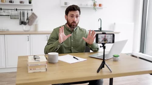 Man Working on Laptop and Recording Video on Smartphone