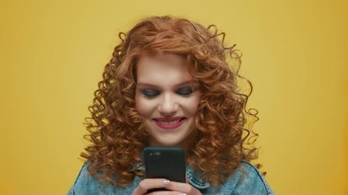 Smiling woman types on phone against yellow backdrop