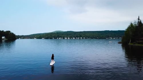A women paddles out towards the center of the lake. The camera pushes in and pans right until the wo