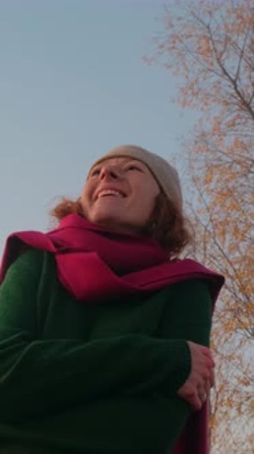 Smiling Woman in Warm Clothing Enjoying a Serene Outdoor Moment with Clear Sky and Trees