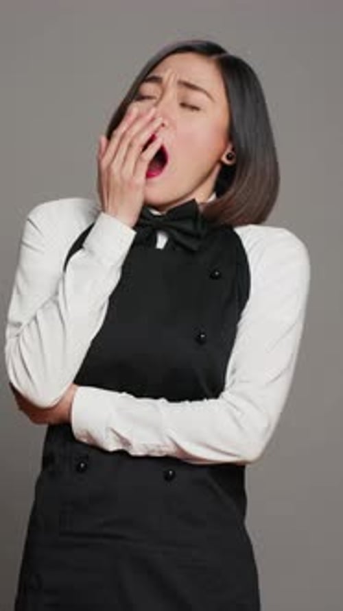 Vertical Video Exhausted Waitress with Apron Yawning Over Grey Background