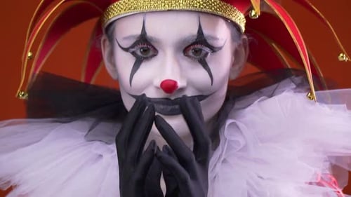 Narrenmädchen mit Make-up und einem großen roten Hut mit Glocken berührt ihre Finger zusammen und lächelt