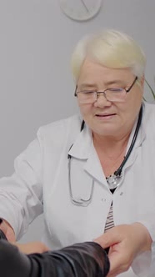 Mature Doctor Examining Patient's Wrist at Clinic