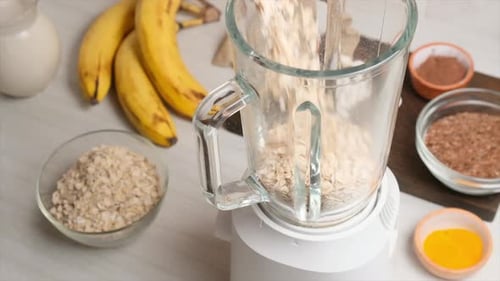 Ganze Haferflocken fallen langsam in einen Glasmixer, um sie zu Mehl zu mahlen oder Hafermilch langsam zuzubereiten