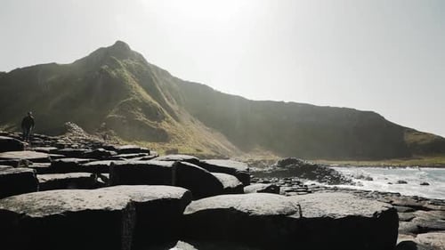 Tourist walking on Giant's Causeway in front of mountainous scenery