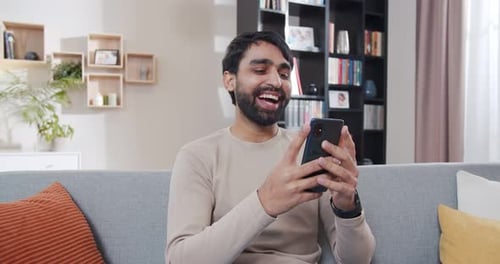 Happy Man Using Smartphone on Couch Indoors
