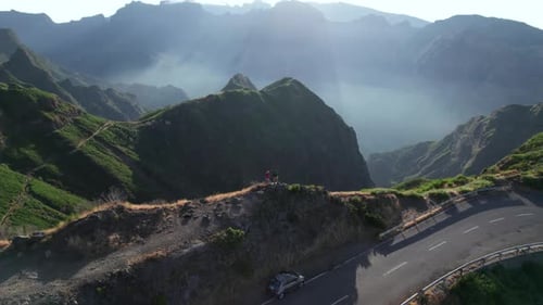 Aerial view of couple stand on top of a mountain viewpoint, green landscape