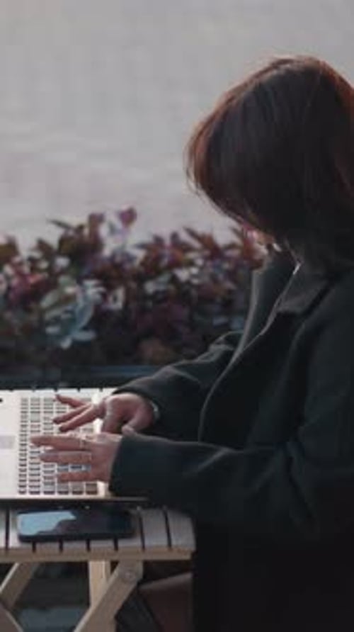 Young Lady Typing on Laptop Outdoors with Phone and Decorative Background