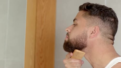 Grooming beard, man using comb in bathroom mirror, focusing on appearance