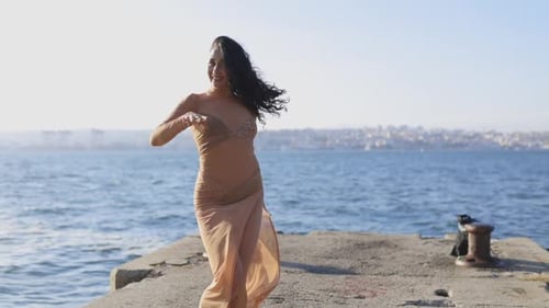 A Woman in a Dress is Dancing on a Pier By the Water