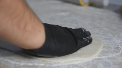 Gloved Hands Flatten Dough on Floury Surface