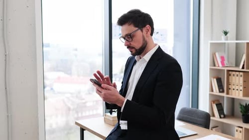 Happy Businessman Using Smartphone in Modern Office Near Window
