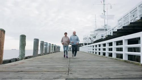 Front View of Senior Couple Running Outdoors on Pier by Sea At