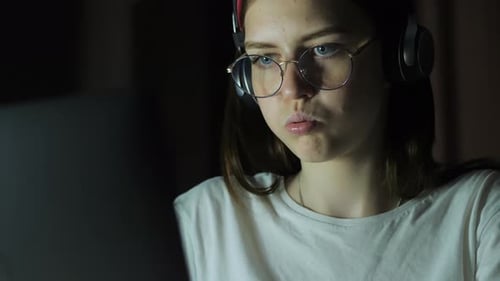 Teenage Girl with Glasses Looks at the Monitor Plays a Game Reads Studies Late at Night