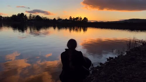 Beobachten Sie den Sonnenuntergang in der Nähe des Sees für ein hockendes Mädchen. Dunkler Himmel mit intensivem, tiefem surrealem Geheimnis. Einsame Frau, Conte