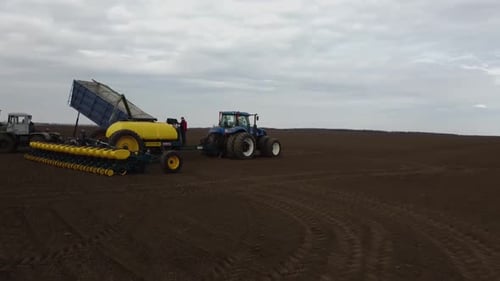 Blue tractor with yellow seeder working on the field in Ukraine OA