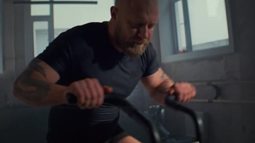 Focused Man Rides Air Bike Trainer with Moving Handles in Gym