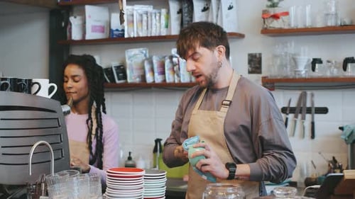 Barista Prepares Coffee While Colleagues Work at Cafe During the Day with Customers Enjoying the