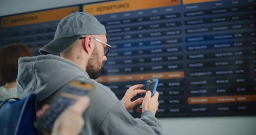 Male Passenger Looking for Flight on Digital Arrival and Departure Information Board Using Phone