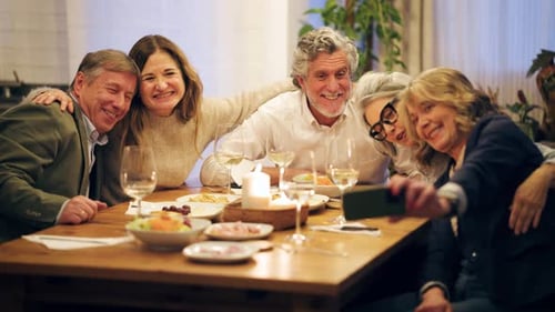 Smiling Adults Gather Around Dinner Table Taking Selfie