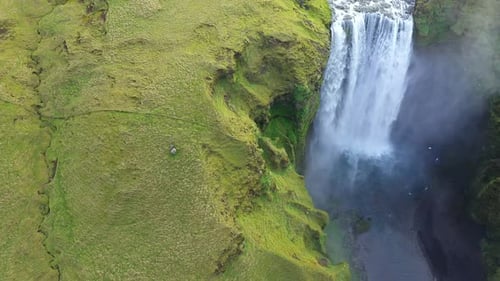 Skogafoss waterfall in the springtime. Vibrant green grass. Slow motion aerial view