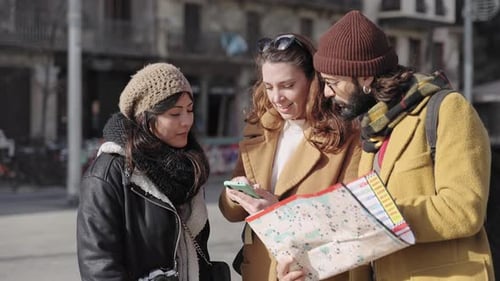 Fröhliche junge Freunde schauen im Winter aufs Smartphone und überprüfen die Richtung des Stadtplans
