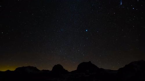 Time lapse or timelapse footage of a starry night or evening sky with bright stars. Mountain silhoue