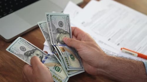 Male Accountant Counts Stack of Dollar Banknotes Before Process of Filing Out Tax Declarations