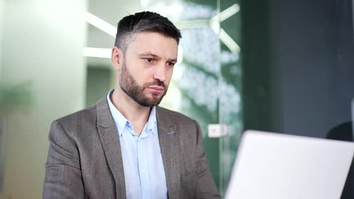 Serious thoughtful businessman works on laptop sitting at workplace in business office. Manager man