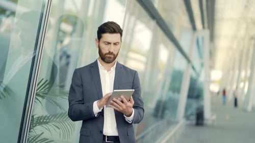 stylish bearded businessman in formal business suit standing working with tablet in hands