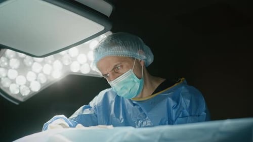 Surgeons in scrubs perform operation under bright surgical light