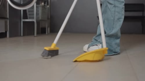 Employer Sweeping Floor with Broom and Dustpan Inside Laundromat