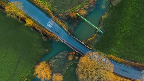 Car Driving Across Small Countryside Bridge Above Winding River and Green Fields Top Down View